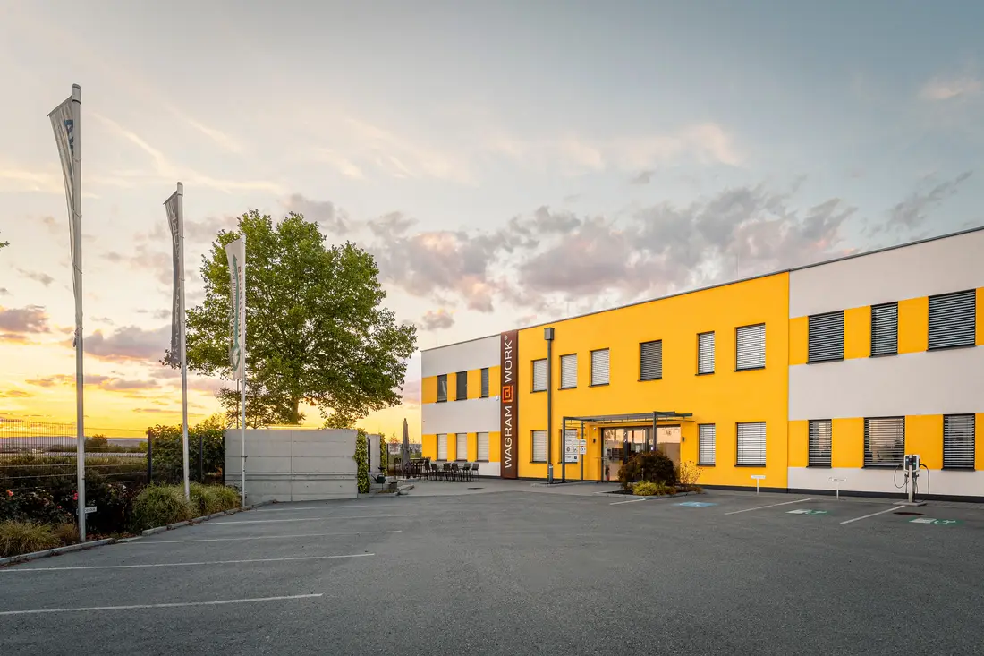 Bürogebäude Wagram@Work in Grafenwörth im Abendlicht, davor Fahnen und der Parkplatz