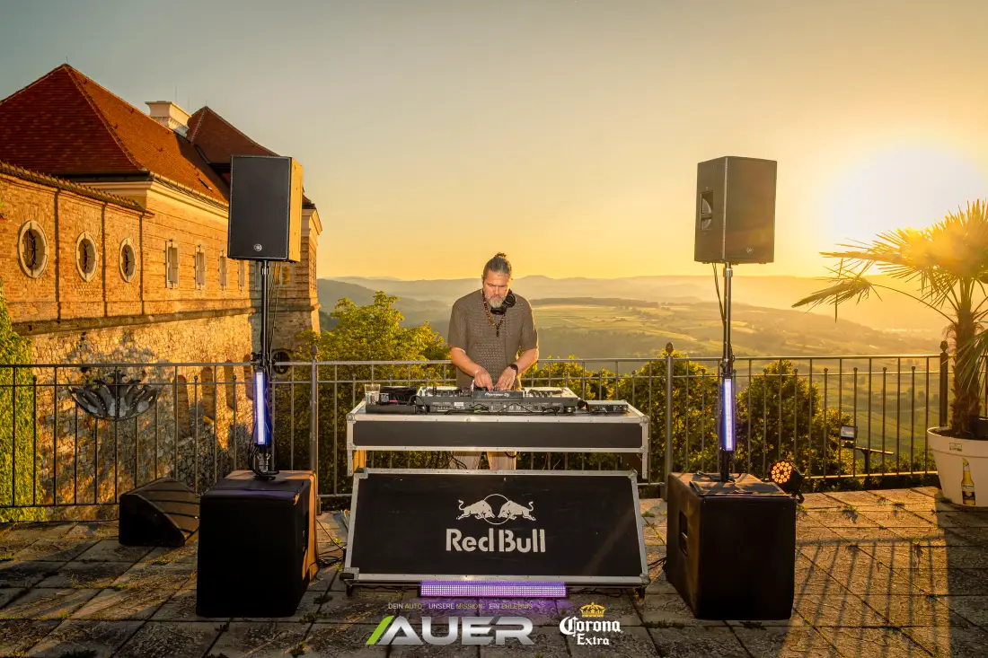 DJ legt bei Sonnenuntergang auf einer Terrasse mit Fernblick auf