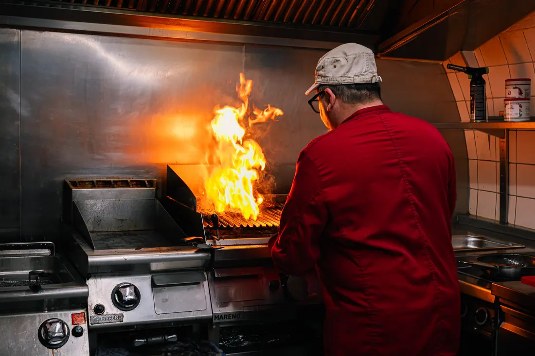 Chef at the grill with a tall flame in a restaurant kitchen