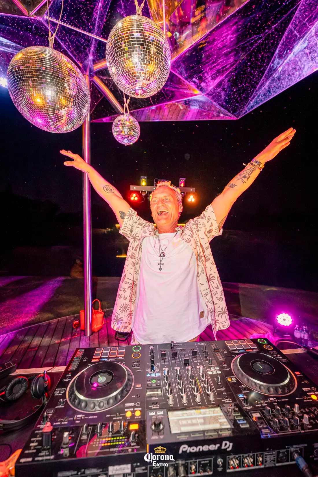 DJ mit ausgebreiteten Armen unter Discokugeln bei Nacht