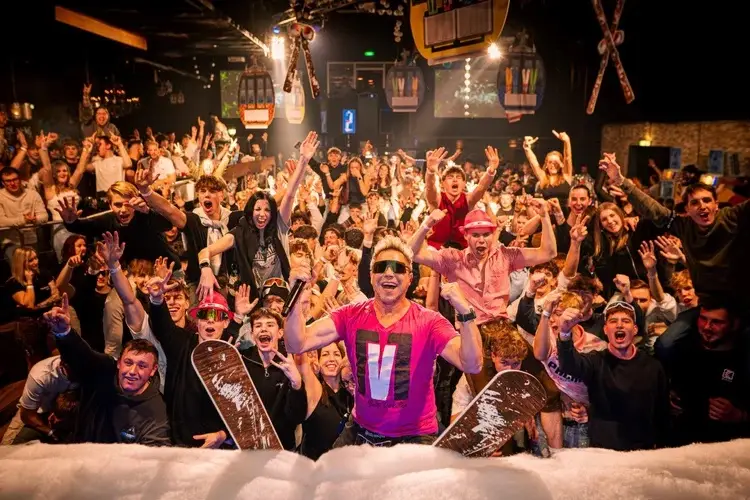 Feiernde Menge bei der Après-Ski-Party mit Snowboards und Gondeln als Deko