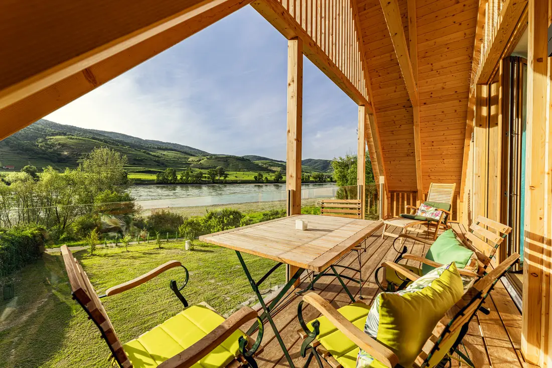 Überdachte Holzterrasse mit Tisch und Liegestühlen, Blick auf die Donau