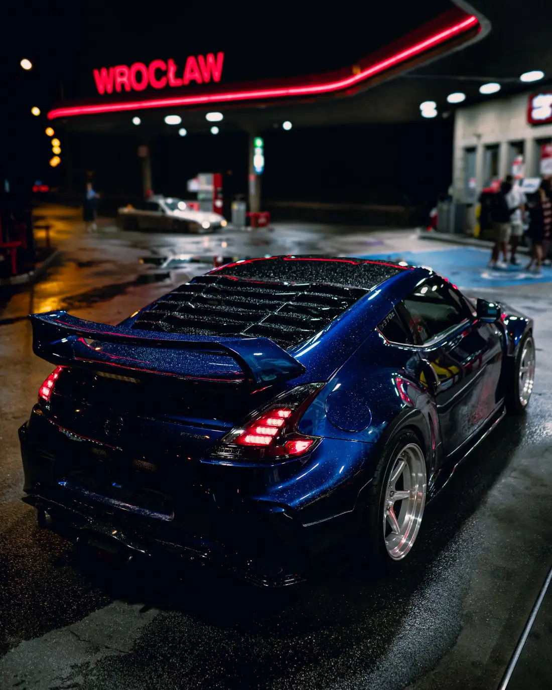 Heck eines blauen Sportwagens bei Nacht an einer Tankstelle