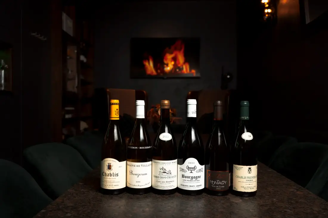 Six wine bottles on a table in front of an open fire