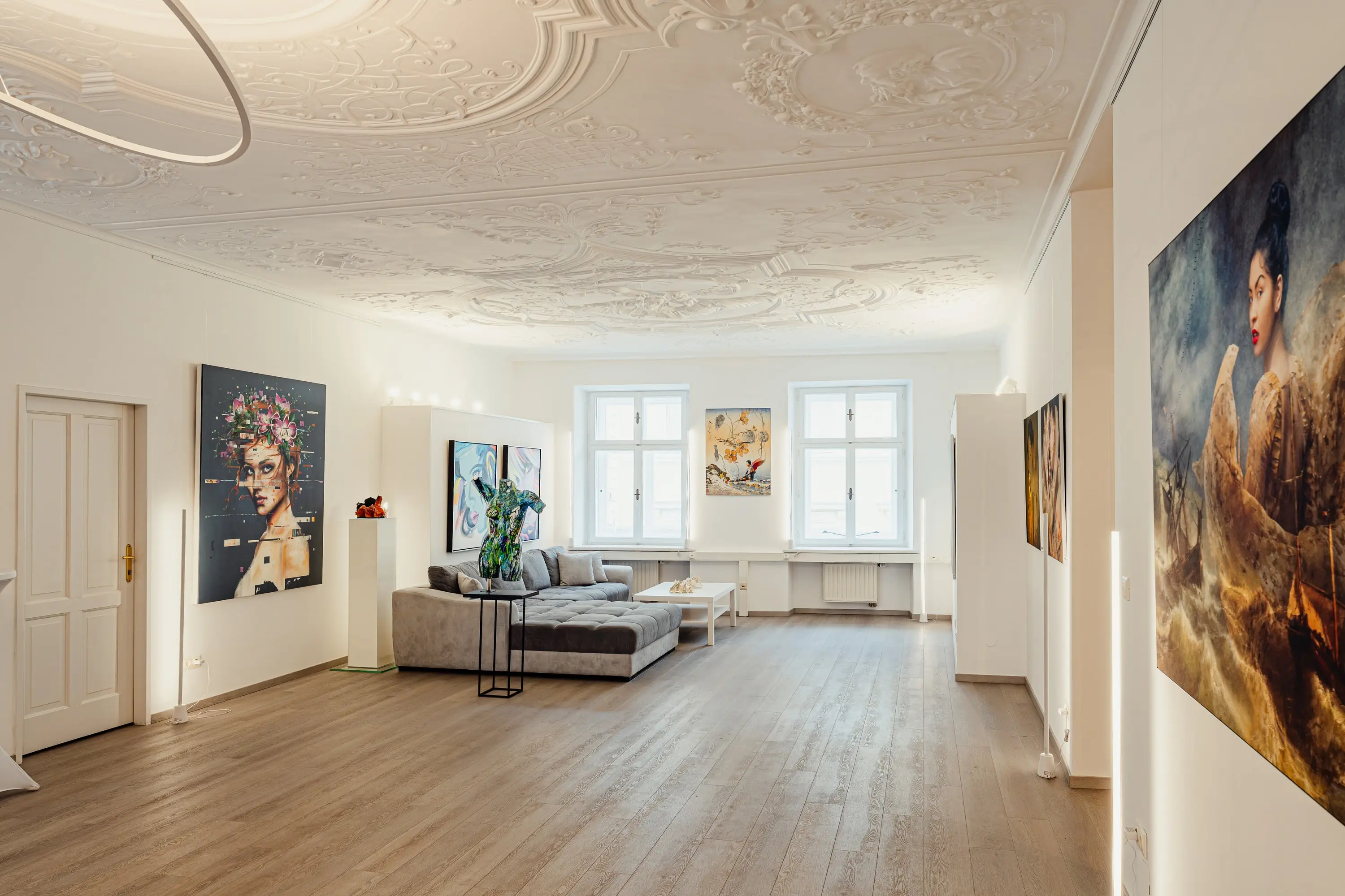 Bright period room with stucco ceiling, parquet floor and large paintings on the walls