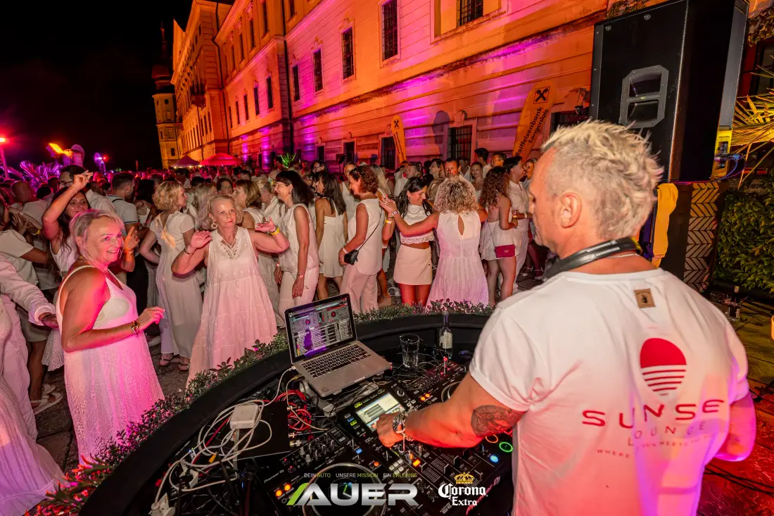 Weiß gekleidete Gäste tanzen vor dem DJ-Pult