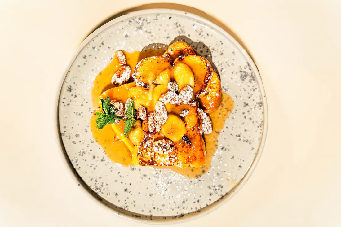 Dessert with caramelised fruit, flaked almonds and mint on a speckled plate, shot from above