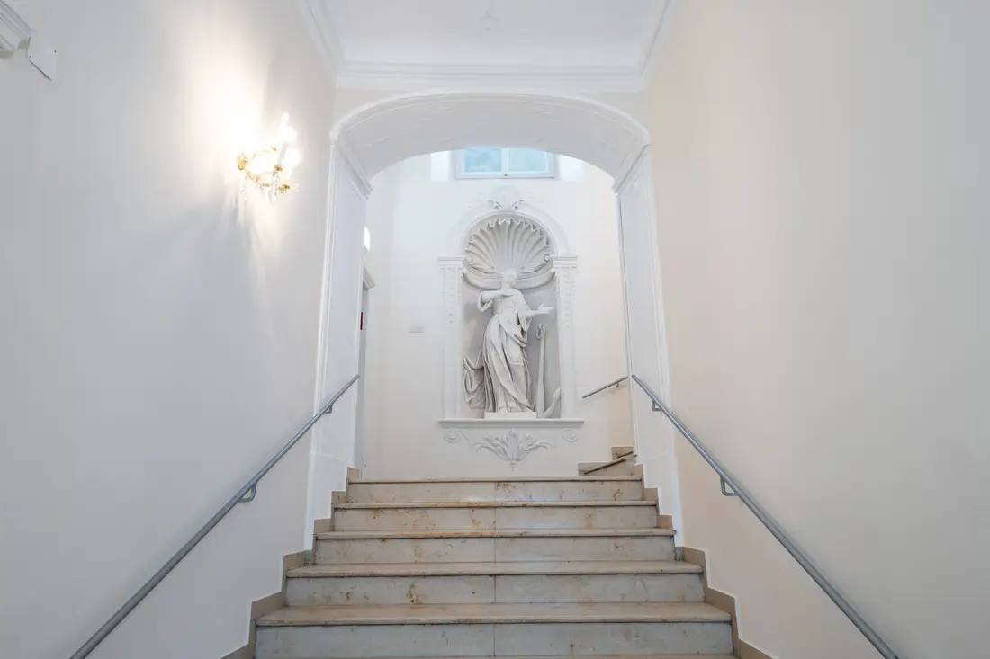 Historisches Stiegenhaus mit Steintreppe und einer Statue in einer Wandnische
