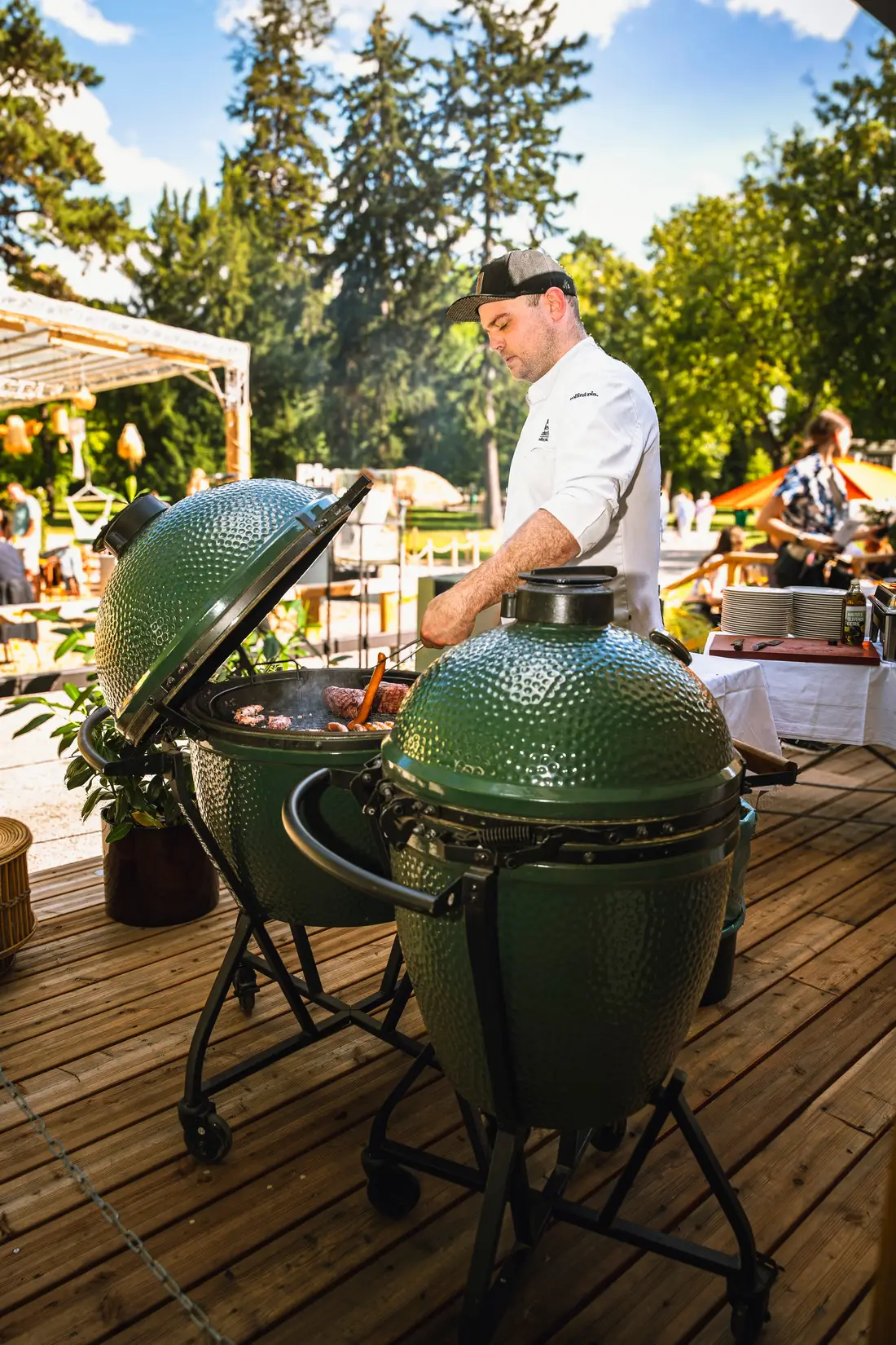 Chef at two green ceramic grills on a wooden terrace