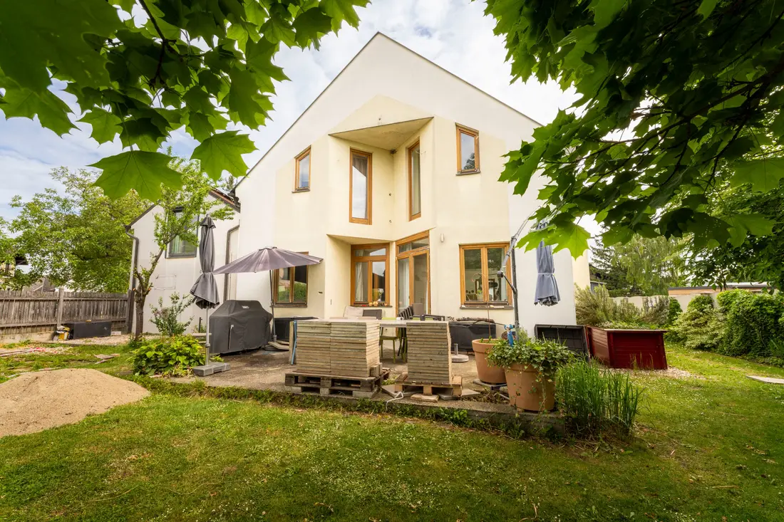 Weißes Einfamilienhaus mit Terrasse und Garten, eingerahmt von Laub