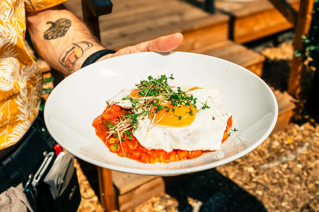 Plate with fried egg on tomato sauce and cress, held by a tattooed arm