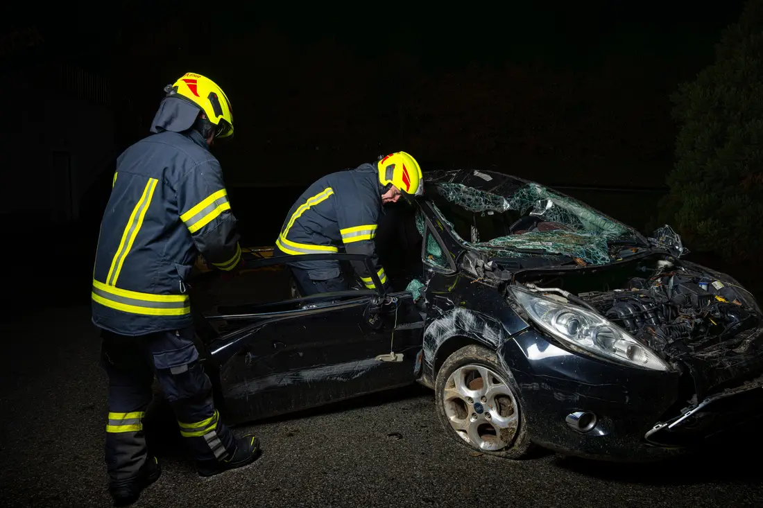 Two firefighters working on a wrecked car at night