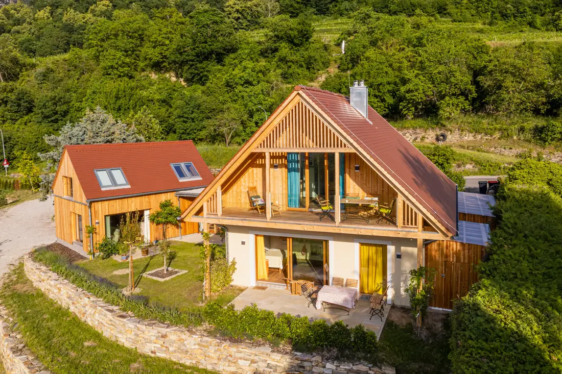 Luftaufnahme zweier Holzhäuser mit Terrasse und Garten an einem Hang mit Trockensteinmauer