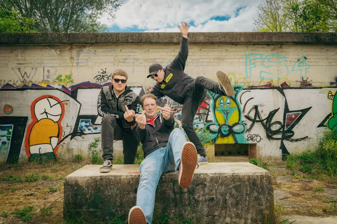 Three young men posing in front of a graffiti wall