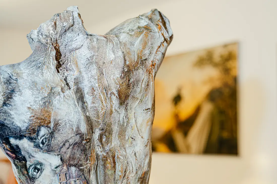 Close-up of a painted torso sculpture, a painting blurred in the background
