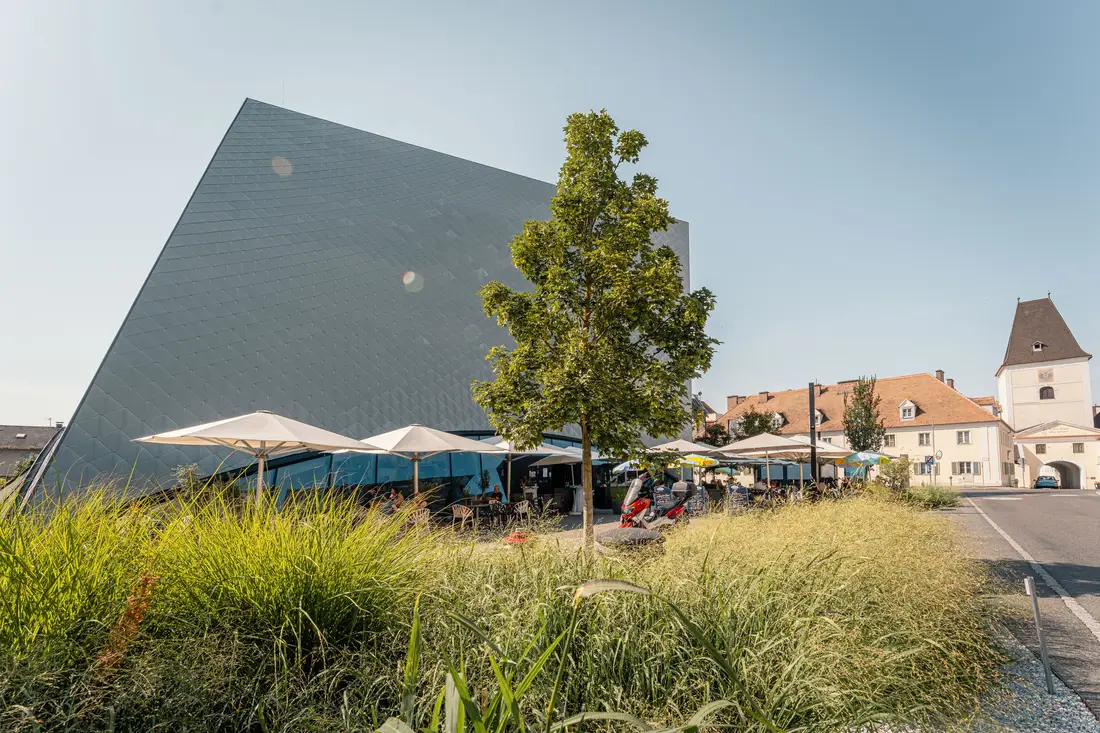 Schindelfassade der Landesgalerie Niederösterreich in Krems, davor ein Gastgarten mit Sonnenschirmen