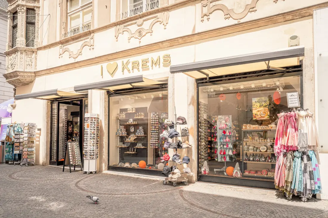 Geschäft mit dem Schriftzug „I love Krems“, davor Ständer mit Hüten, Tüchern und Postkarten