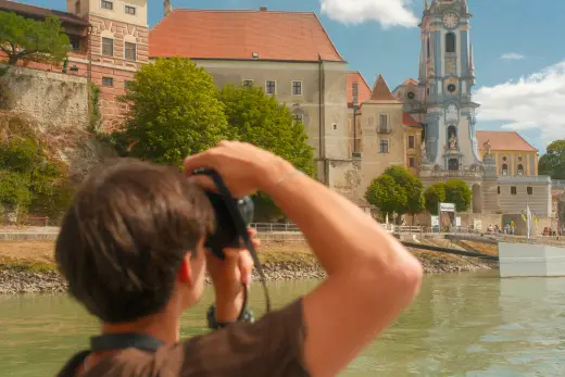 Blick über die Schulter eines Fotografen auf eine Kirche mit blauem Turm an der Donau