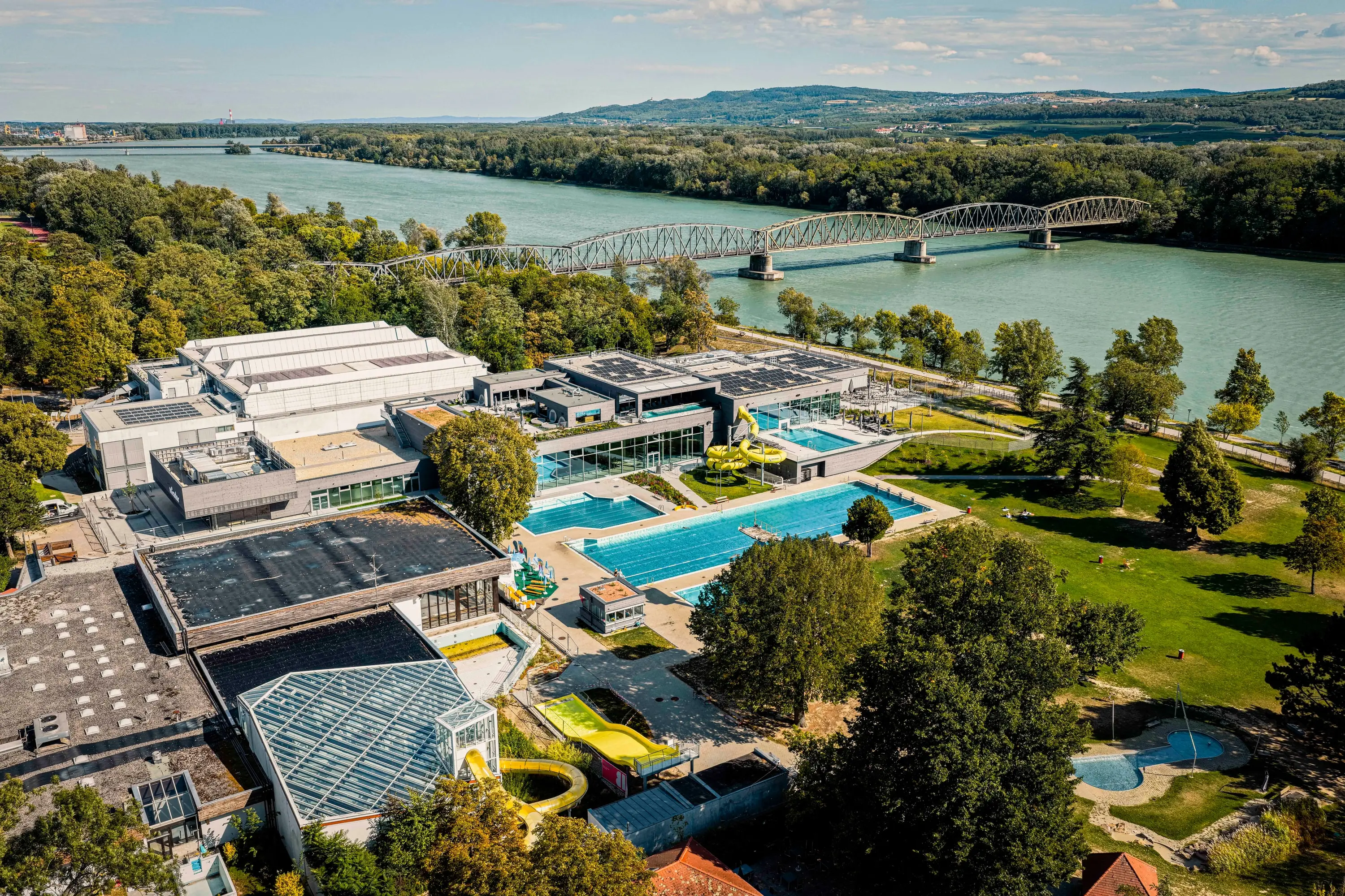 Luftaufnahme des Bads Mirador in Krems an der Donau mit Hallenbad, Freibecken und Brücke im Hintergrund