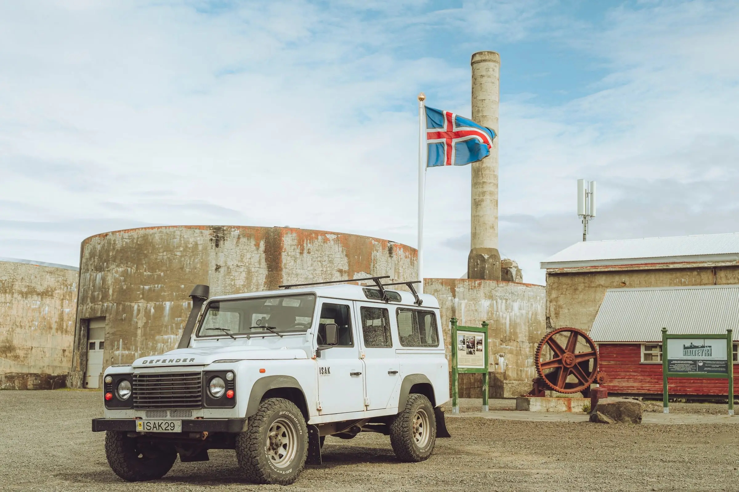 Weißer Land Rover Defender vor alten Fabrikgebäuden mit isländischer Flagge