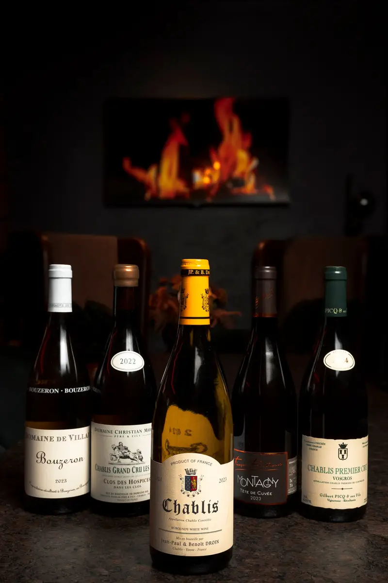 Weinflaschen auf einem Tisch, vorne eine Flasche Chablis, dahinter ein Kaminfeuer
