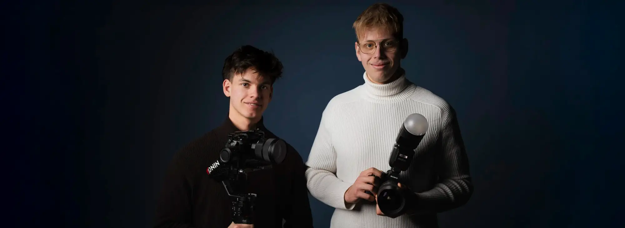 Paul Schneider und Bryan Schmied mit Kameras vor dunkelblauem Hintergrund