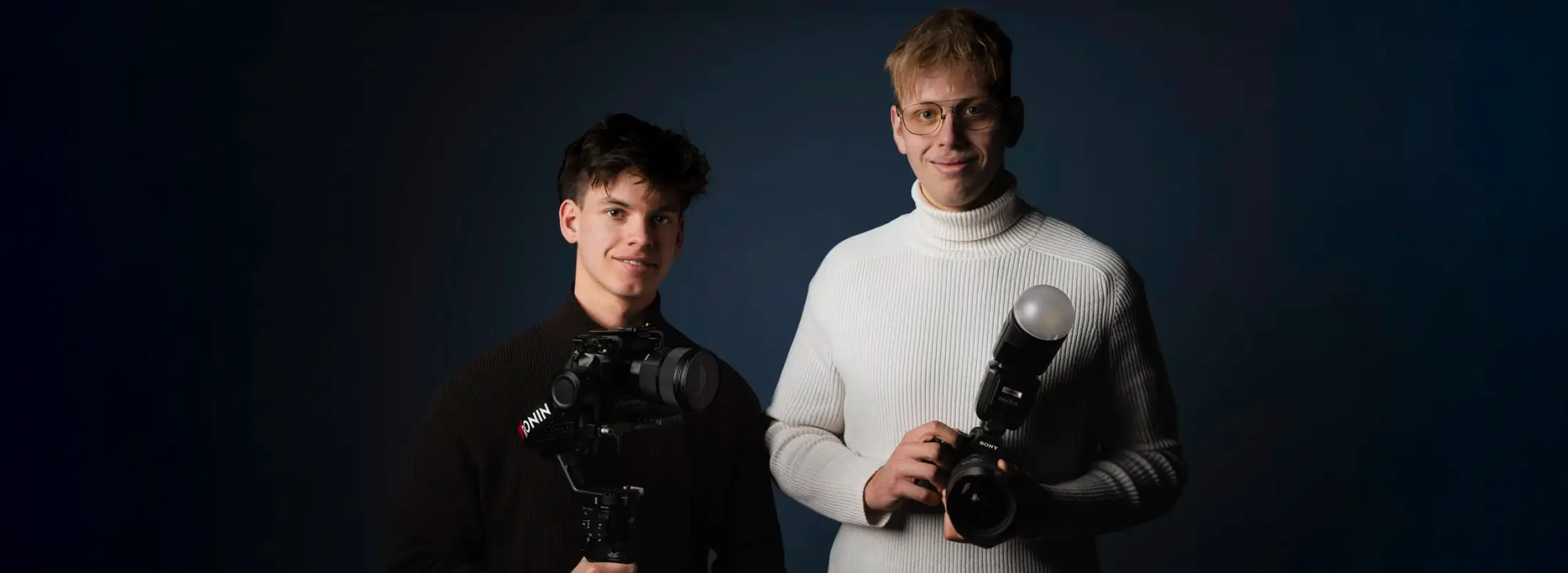 Paul Schneider und Bryan Schmied mit Kameras vor dunkelblauem Hintergrund